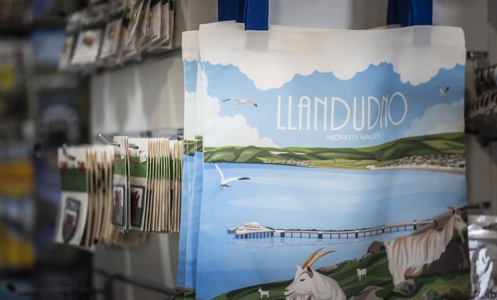 Reusable Llandudno shopping bags featuring an illustrated North Wales coastal design displayed in the gift shop.